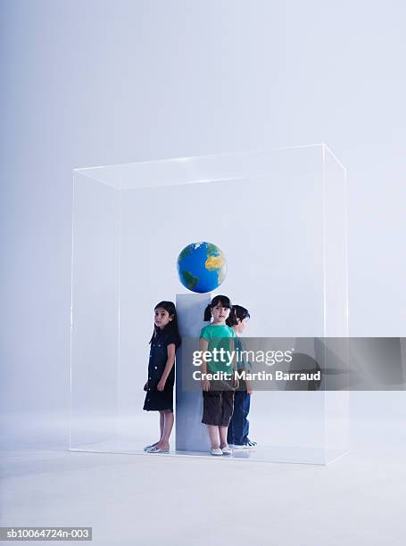 three children (4-9) standing in glass cabinet with globe - glass box stock pictures, royalty-free photos & images