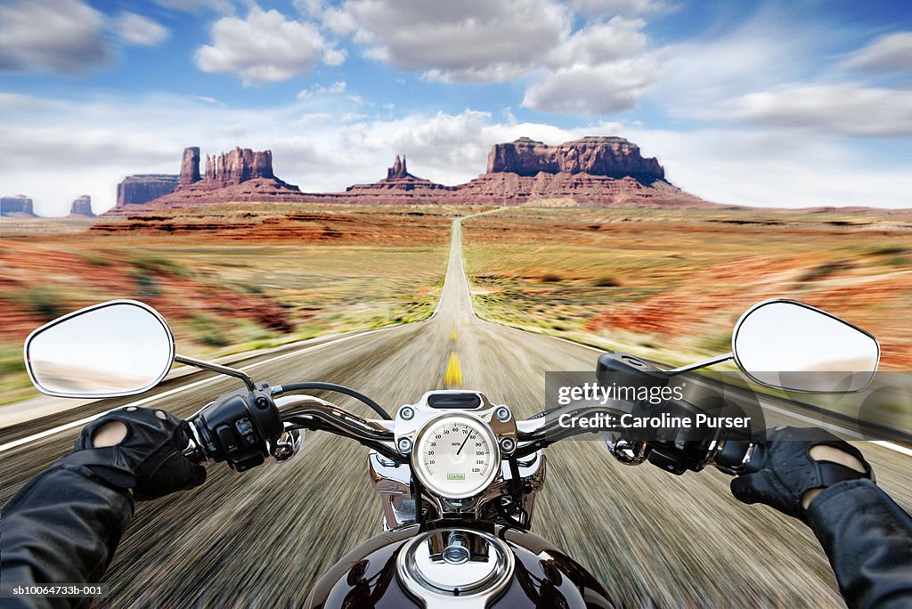 Man riding motorbike on dirt track, Monument valley in background (zoom)