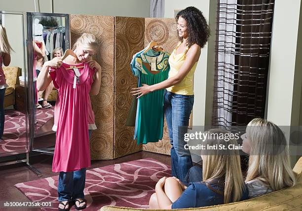 teenage girls (14-15) modelling clothes for friends outside dressing room, with sales clerk holding up options - girl changing room shop stock pictures, royalty-free photos & images