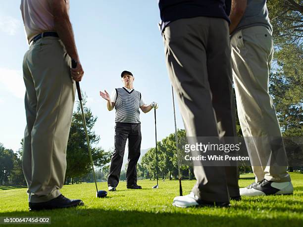 four male golfers talking, leaning on clubs, surface level - golfer stock pictures, royalty-free photos & images