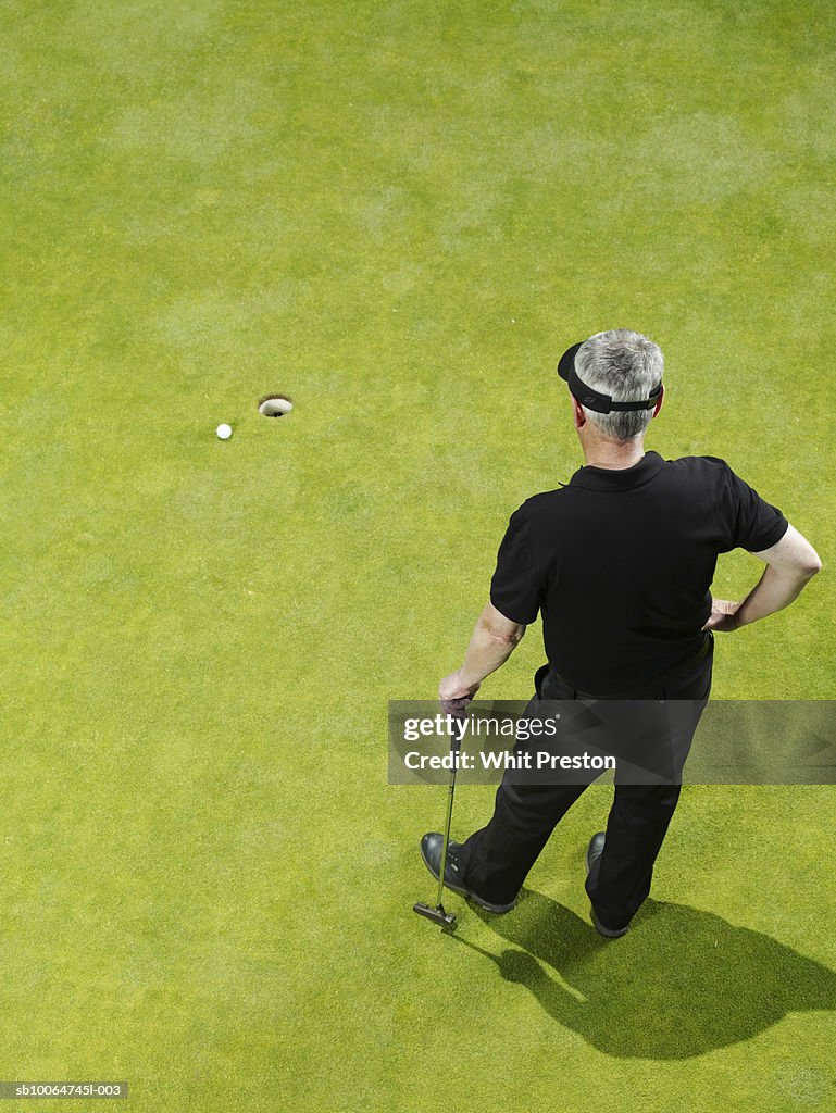 Mature golfer looking at hole, hand on hip, rear view