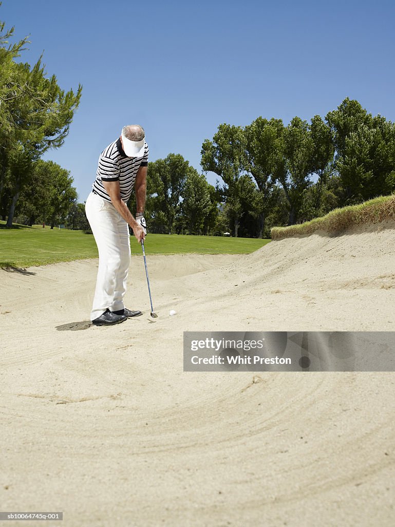 Male golfer putting ball from sand trap