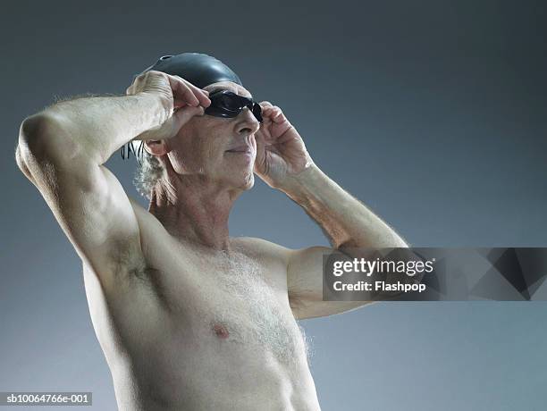 senior man putting on swimming goggles, studio shot - senior swimming stock pictures, royalty-free photos & images