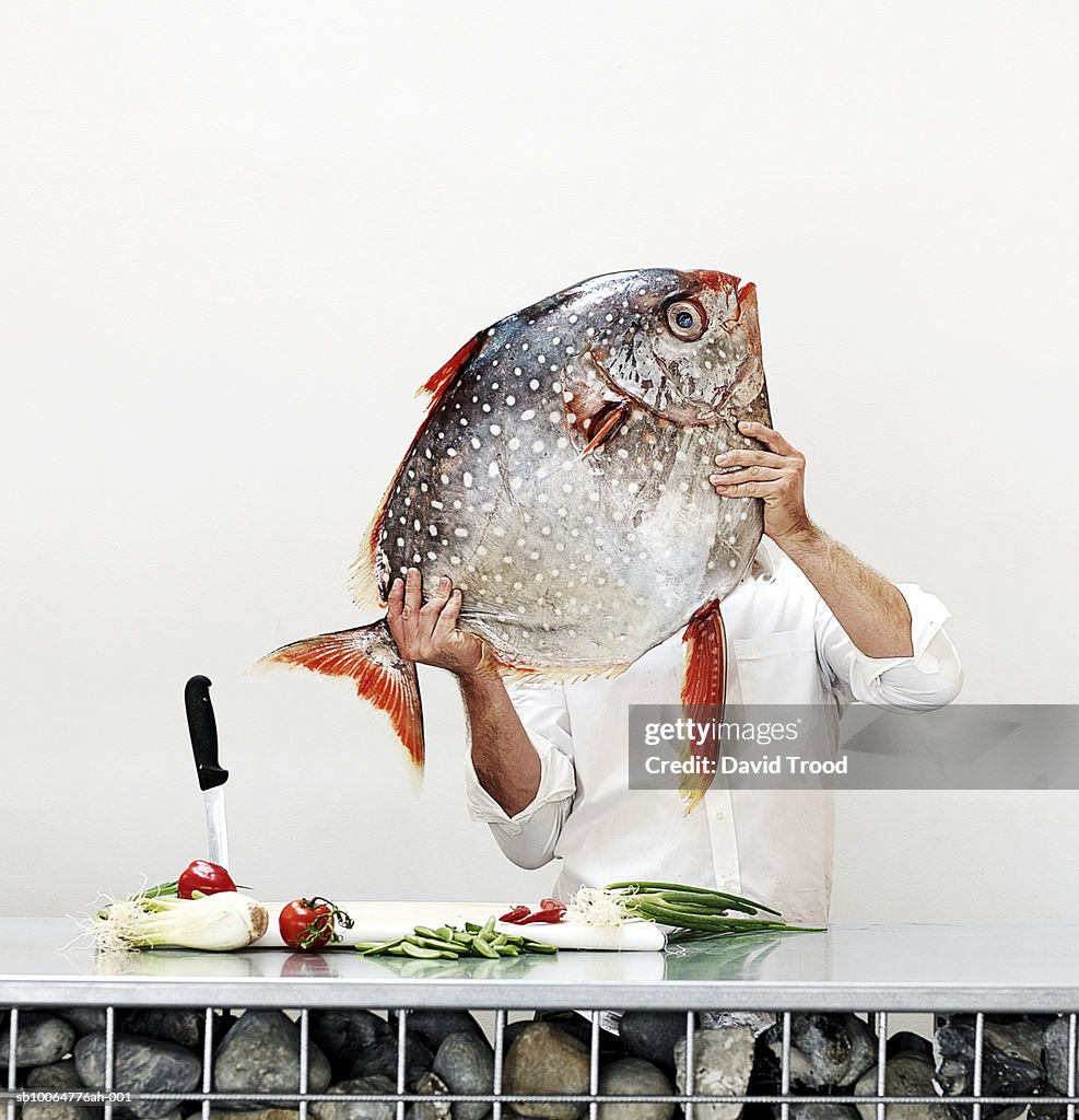 Chef holding big fish in commercial kitchen, obscured face, studio shot