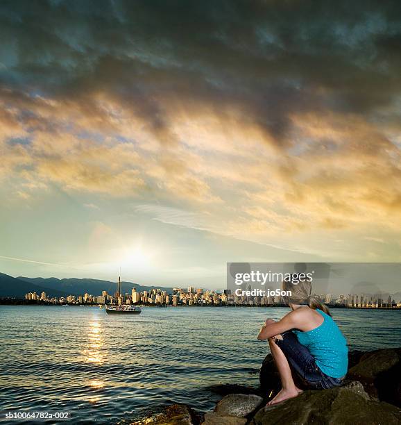 teenage girl (13-14) sitting by water looking at city skyline at sunset - vancouver skyline stock pictures, royalty-free photos & images