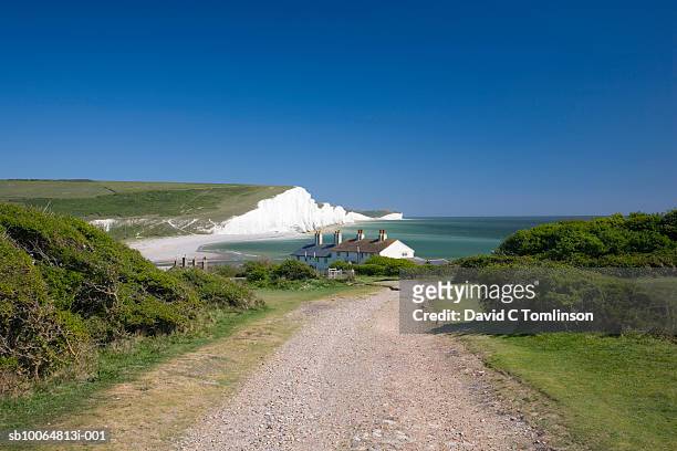 view along coastal path towards houses and the seven sisters cliffs, seaford head, sussex, england, uk - seven sisters cliffs stockfoto's en -beelden