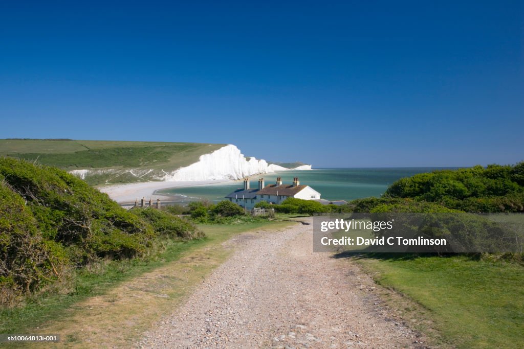 View along coastal path towards houses and the Seven Sisters cliffs, Seaford Head, Sussex, England, UK