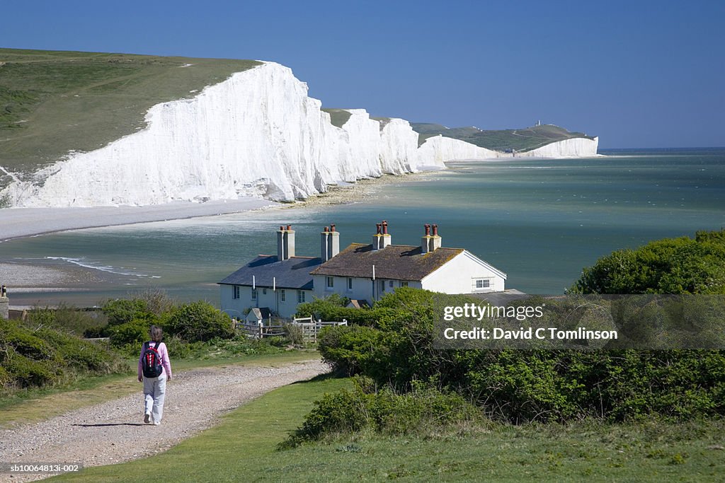 Person walking towards houses and the Seven Sisters cliffs, Seaford Head, Sussex, England, UK