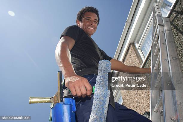 man on ladder, cleaning window, smiling, low angle view - washing windows stock pictures, royalty-free photos & images