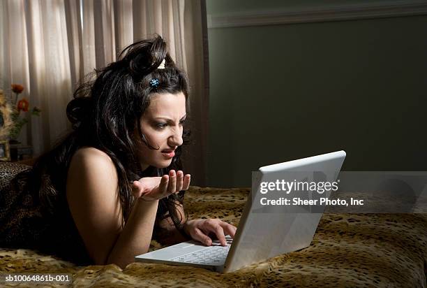 young woman lying on bed, using laptop and gesturing - leopard print stock pictures, royalty-free photos & images