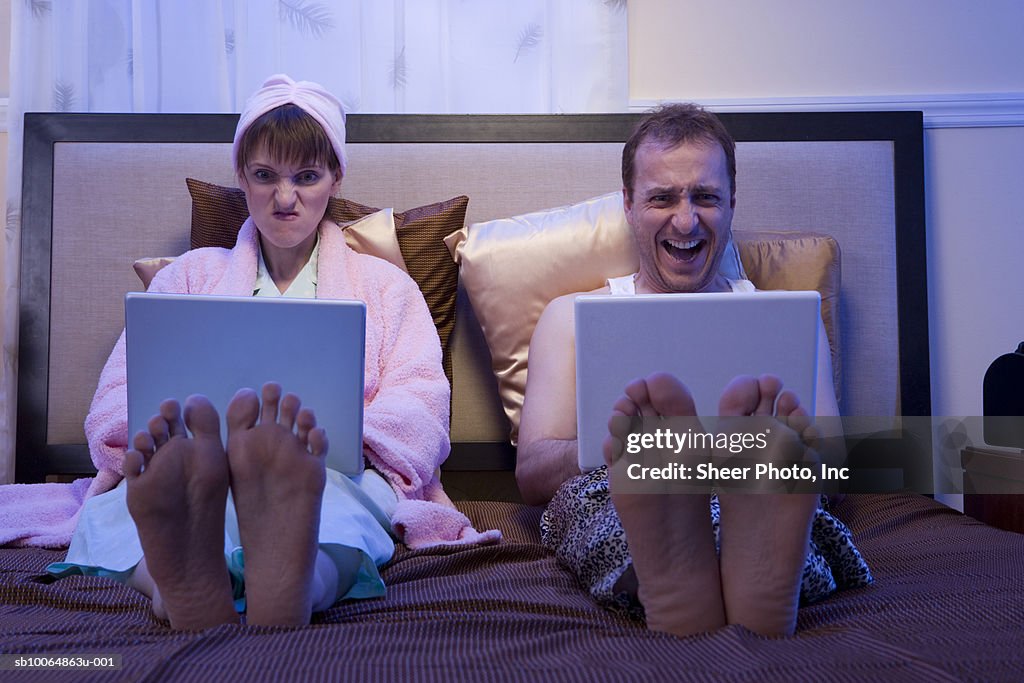 Couple using laptops side by side in bed