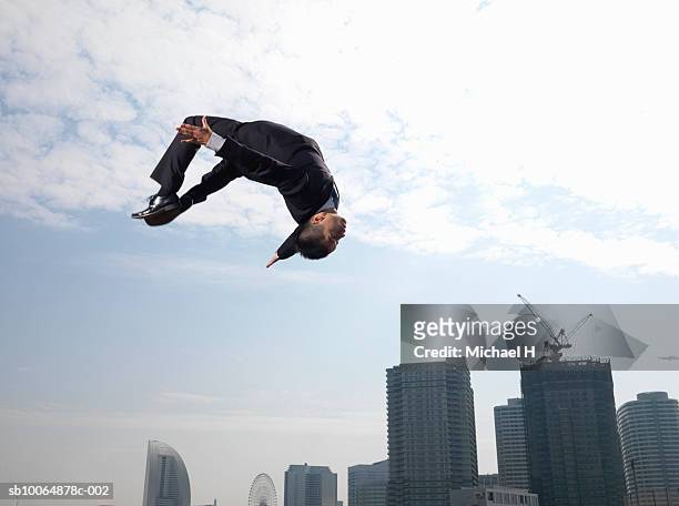 businessman doing somersault, skyscrapers in background, low angle view - backflipping imagens e fotografias de stock