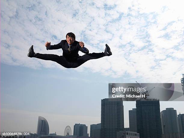 businessman jumping in air, skyscrapers in background, low angle view - legs apart imagens e fotografias de stock