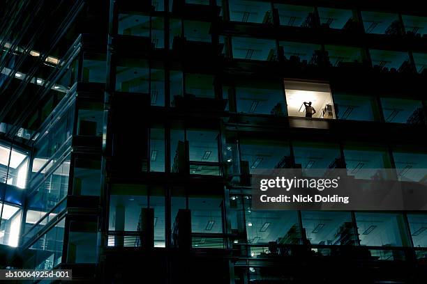 office building at night, man standing in one illuminated window, low angle view - 窓辺　夜 ストックフォトと画像