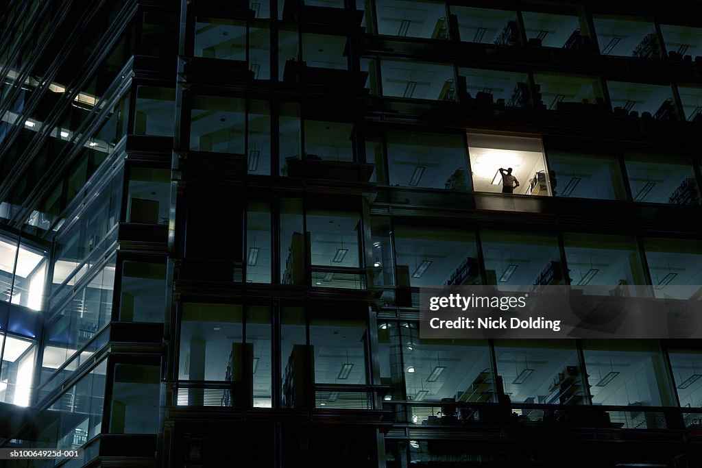 Office building at night, man standing in one illuminated window, low angle view