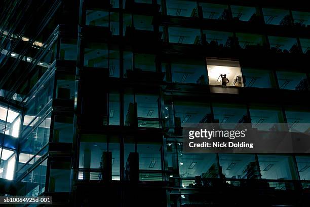 Office building at night, man standing in one illuminated window, low angle view