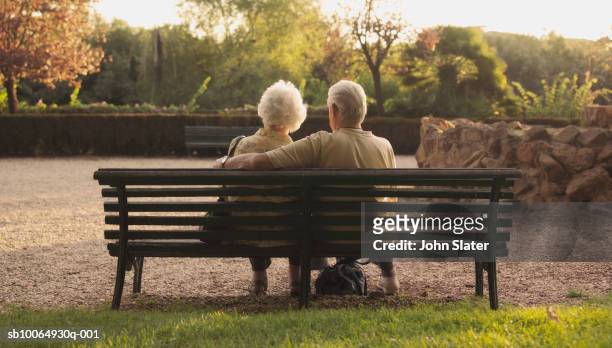 senior couple sitting on bench in park, rear view - pensioen thema stockfoto's en -beelden