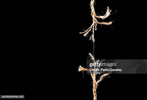 frayed rope breaking on black background - fragility fracture stock pictures, royalty-free photos & images