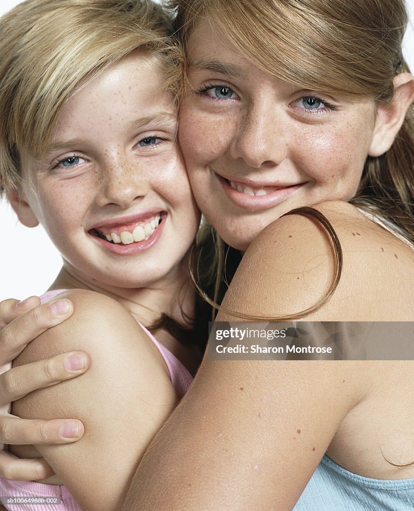 Two girls (10-14) embracing, smiling, portrait, close-up