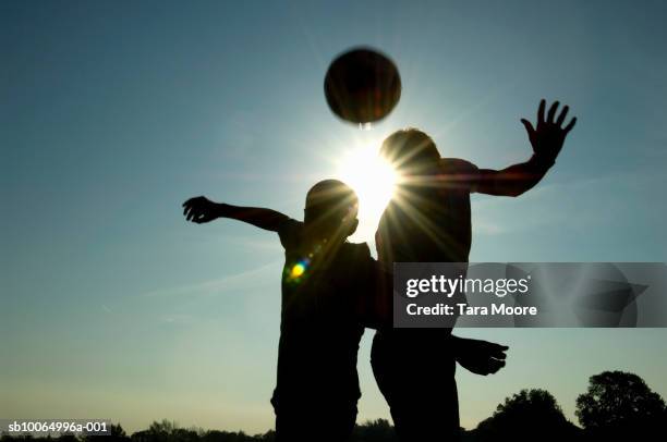 silhouette of two people playing football - kopfball stock-fotos und bilder