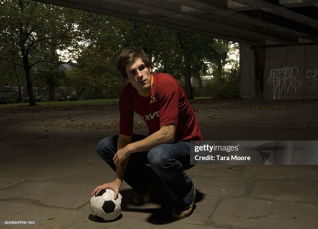 Man crouching with football under elevated road