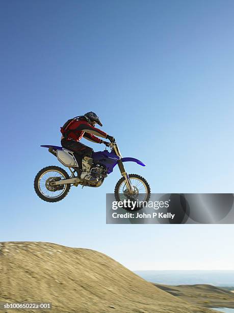 motocross rider catching air in desert terrain, side view - motorcycle stunt stock pictures, royalty-free photos & images