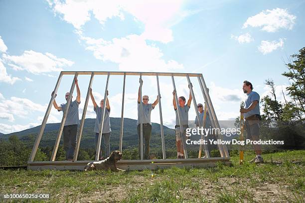 construction workers lifting up wooden frame of house - volunteer building stock pictures, royalty-free photos & images