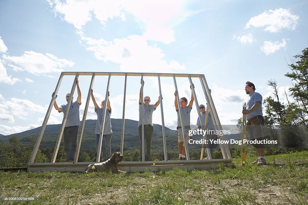 Construction workers lifting up wooden frame of house