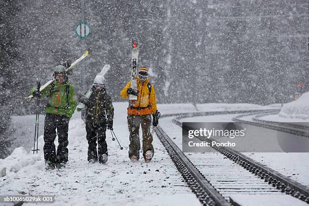 switzerland, davos, three skiers walking along train tracks in snowfall - skikleidung stock-fotos und bilder