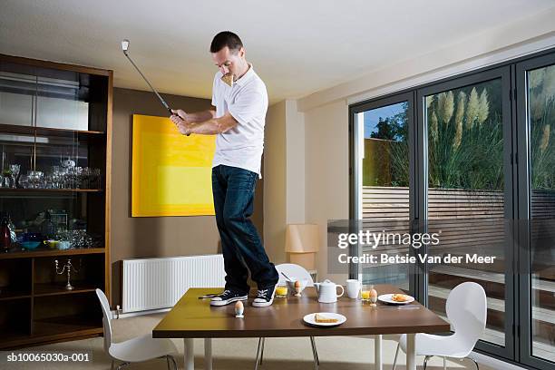 man swinging golf club on dining table - sports man cave stock pictures, royalty-free photos & images