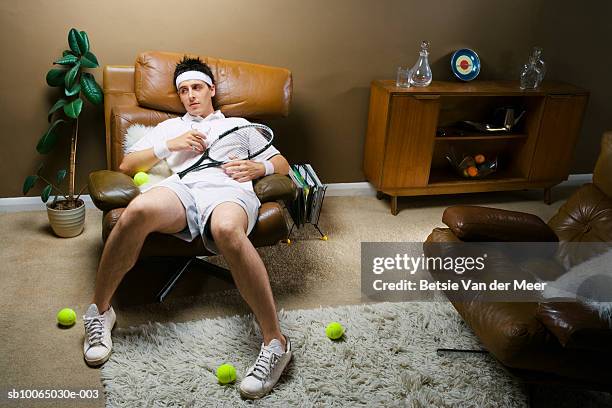 man sitting on sofa with tennis racquet and balls - man cave stock pictures, royalty-free photos & images