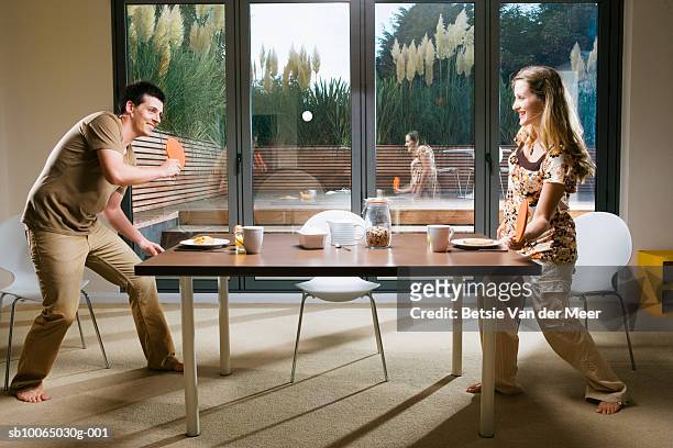 young couple playing table tennis at dining table, smiling, side view - tischtennis spielerin stock-fotos und bilder