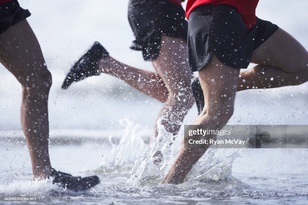 Men running in ocean, low section