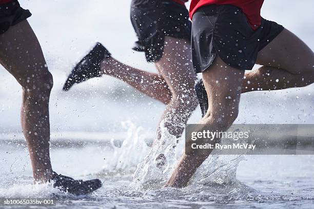 men running in ocean, low section - black shorts stockfoto's en -beelden