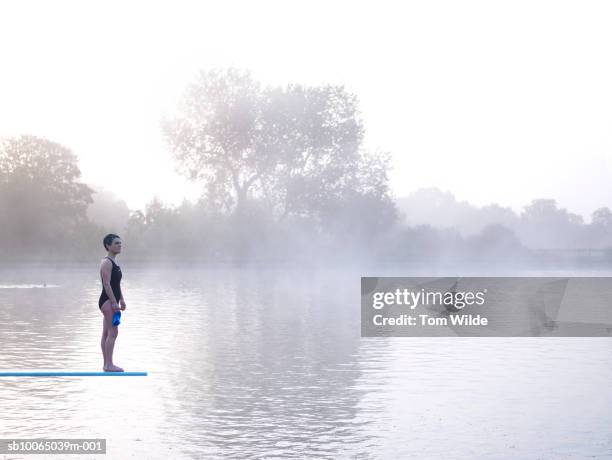 woman standing on diving board by lake - woman diving board stock pictures, royalty-free photos & images