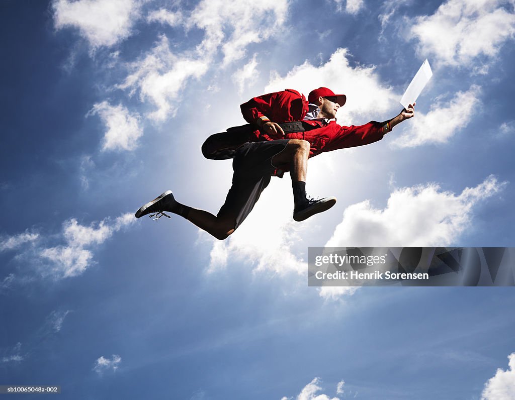 Man flying in air with letter in hand, against sky, low angle view