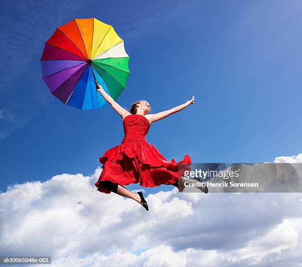 young woman leaping in air, holding umbrella, smiling - multi colored dress stock pictures, royalty-free photos & images