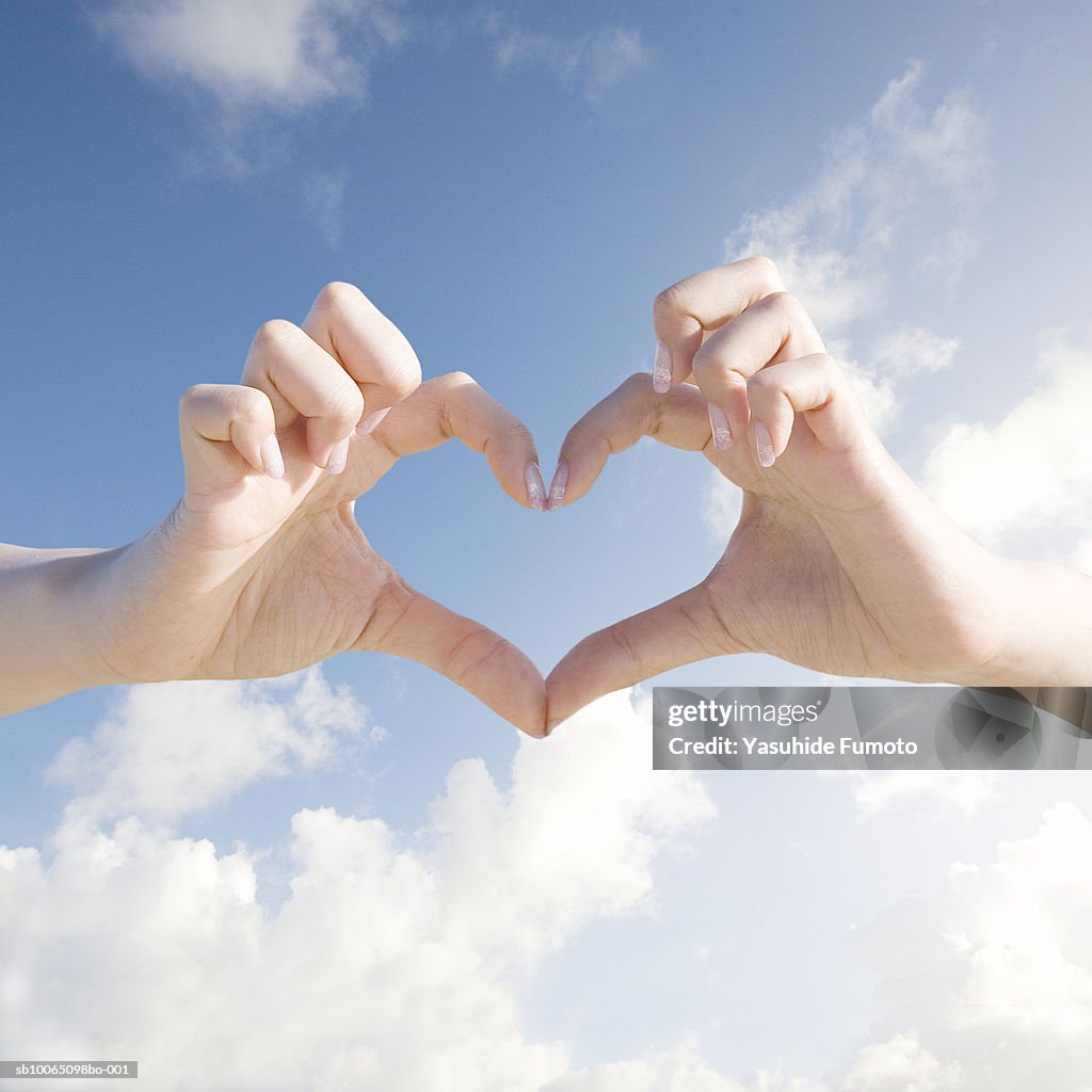 Close-up of woman forming heart shape with hands against sky background