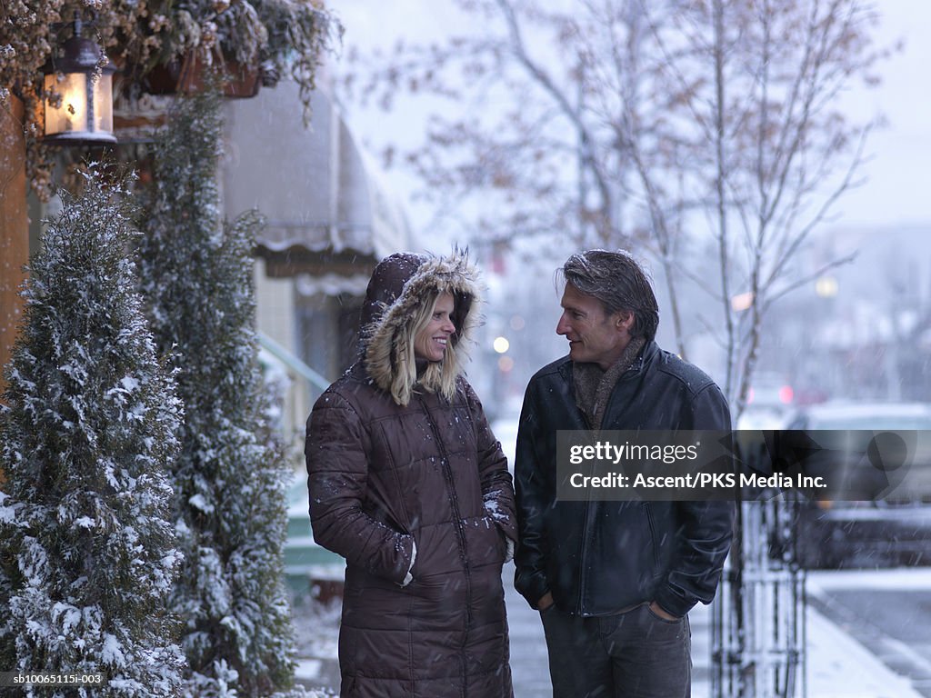 Mature couple walking on street in blizzard, smiling