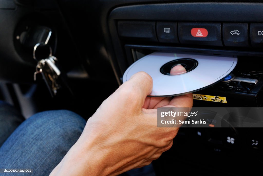 Mature man inserting compact disc into car stereo, close-up of hand