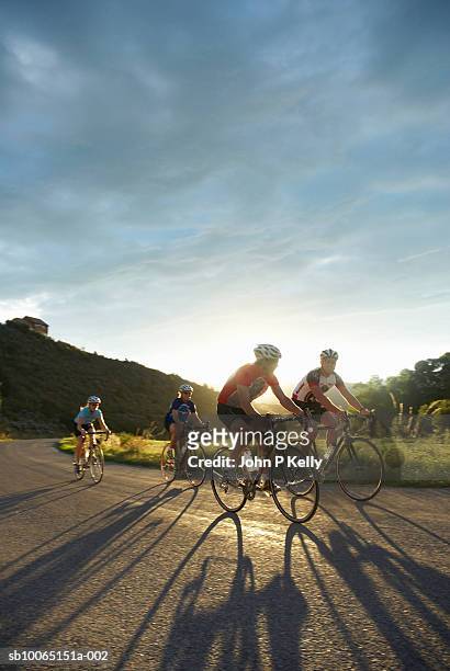 four people riding bicycles on coutry road at sunset - ciclismo gruppo foto e immagini stock