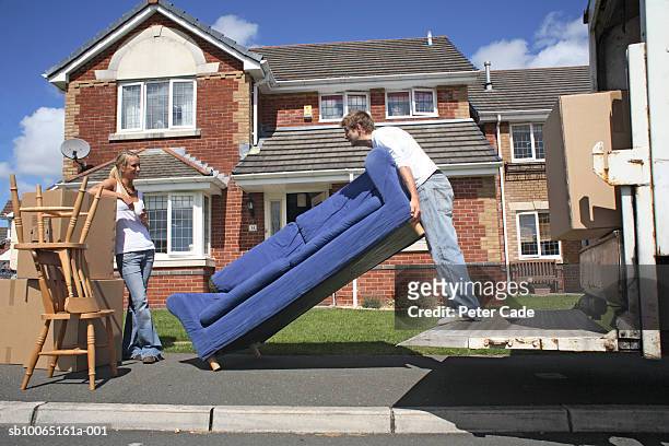 young man lifting sofa standing on truck platform, woman watching standing by, side view - carrying sofa stock pictures, royalty-free photos & images