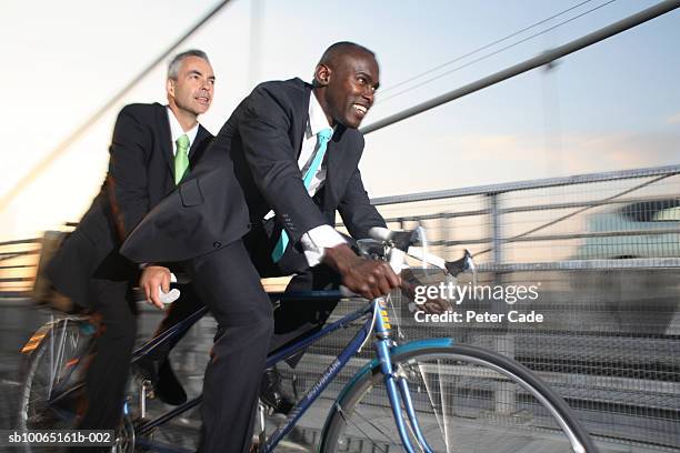 two business men riding on tandem bike on bridge - bicycle tandem stock pictures, royalty-free photos & images