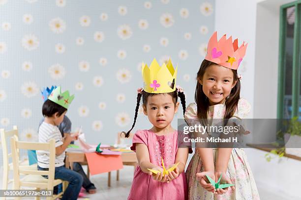 portrait of two girls (4-5) with origami pieces, out of focus boys playing in background - paper crown stock pictures, royalty-free photos & images