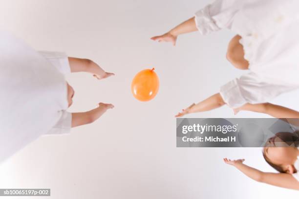 three children (4-5 years) throwing balloon in air, view from below - 4 5 years balloon stock pictures, royalty-free photos & images