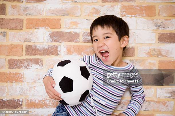 boy (4-5 years) holding toy soccer ball, standing against brick wall, portrait - 4 5 years stock-fotos und bilder