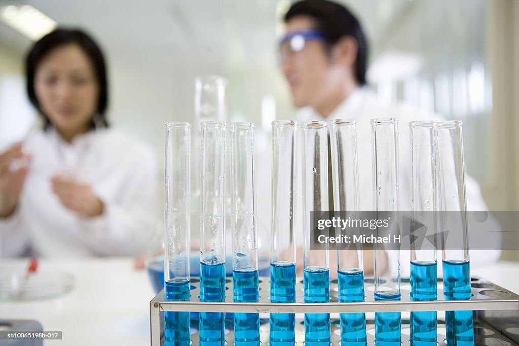 Two researchers working in laboratory, (focus on test tubes in foreground)