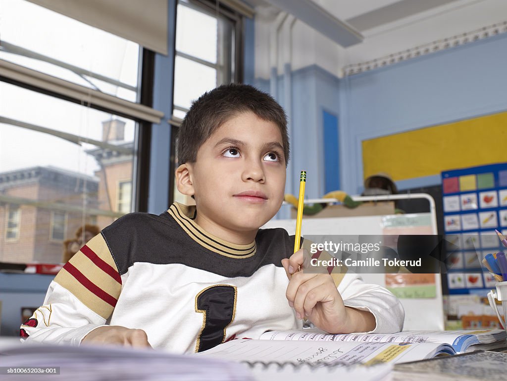 Boy (10-11) doing homework, looking up