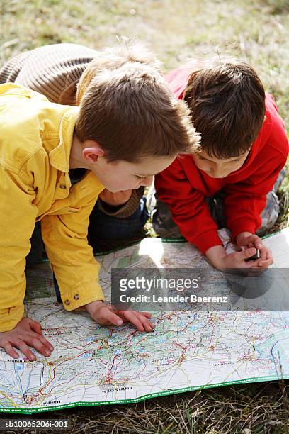 three boys (7-9 years) looking at map on ground, elevated view - orientierungslauf landkarte gruppe stock-fotos und bilder
