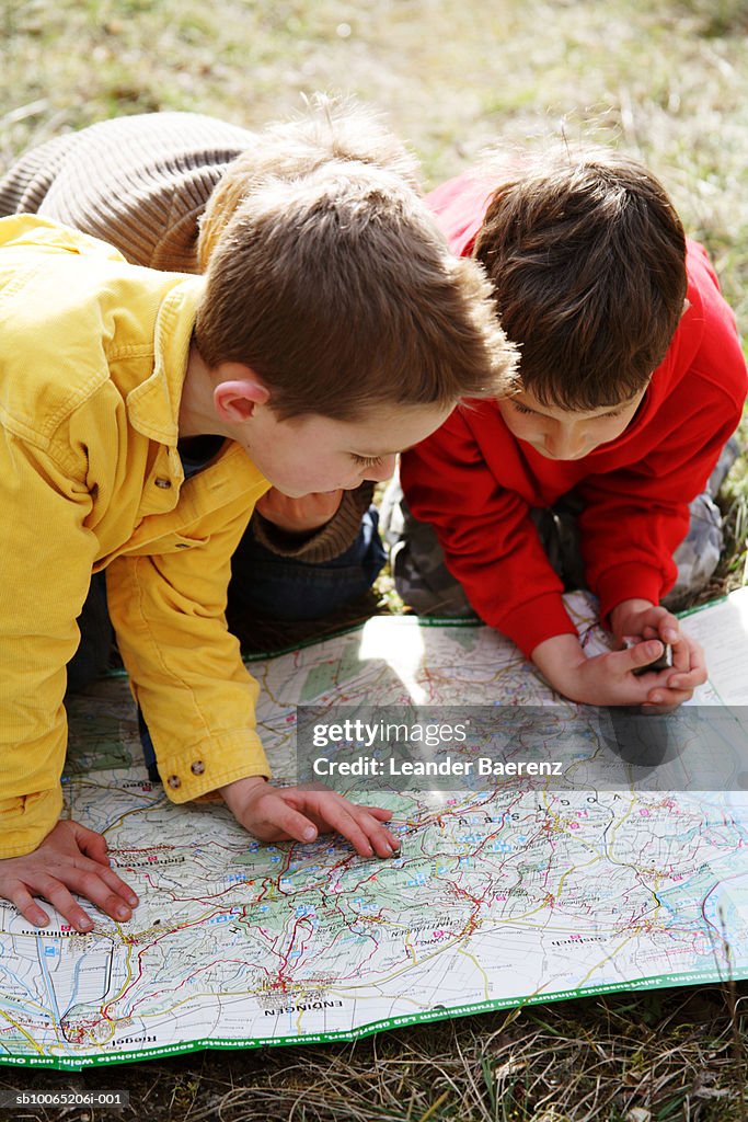 Three boys (7-9 years) looking at map on ground, elevated view